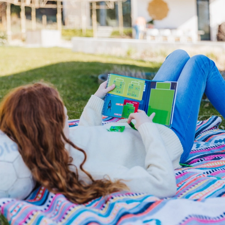 Dziewczynka rozgrywająca partię Goool! na świeżym powietrzu z książeczką z zadaniami.