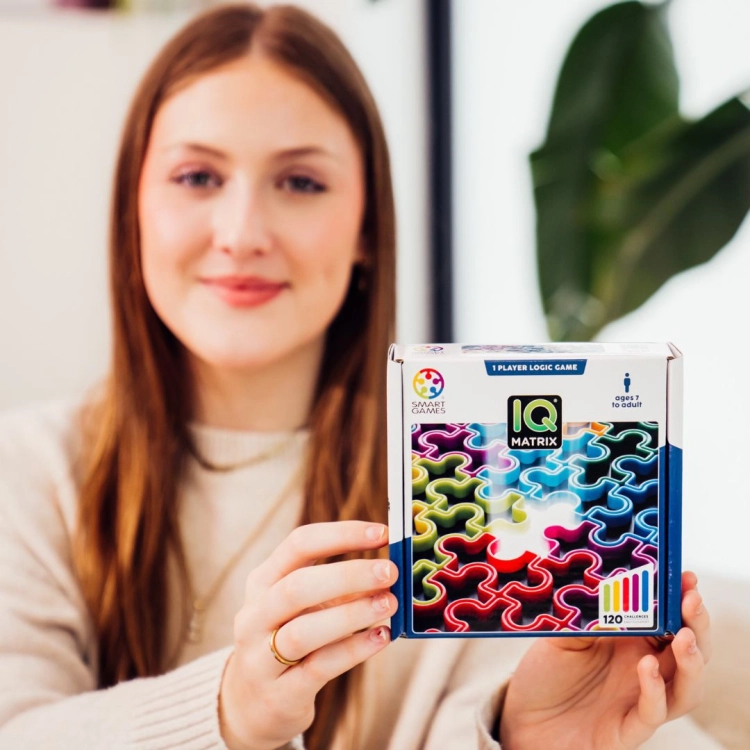 Kobieta prezentująca opakowanie gry IQ Matrix z logo Smart Games.