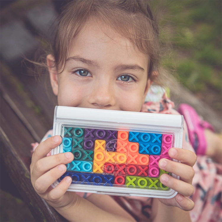 Dziewczynka trzymająca grę IQ XOXO z ułożonymi kolorowymi elementami.