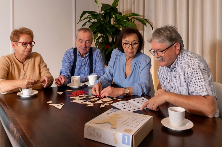 Seniorzy grający w grę logiczną tangram silver przy stole.