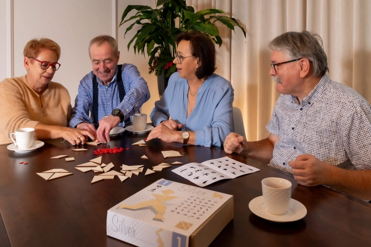 Grupa osób bawiących się grą tangram silver przy stole.
