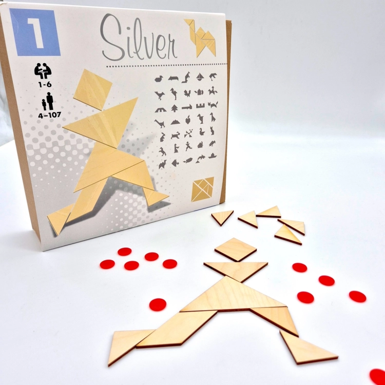 Układanka z elementów tangram silver obok pudełka i czerwonych żetonów na białym tle.