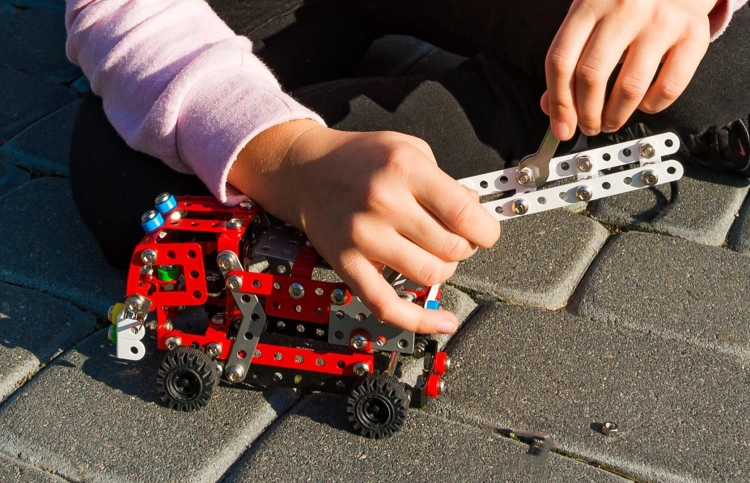 Zbliżenie na dłonie montujące model straży pożarnej z zestawu Mały Konstruktor.