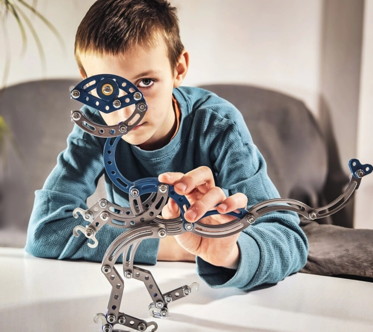 Uśmiechnięty chłopiec trzymający gotowy model dinozaura Velociraptor