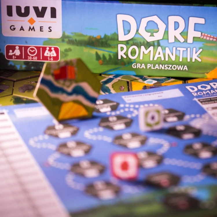 Zbliżenie na elementy gry Dorfromantik – Kolorowe kafelki planszy z torami kolejowymi, domkami i rzeką.