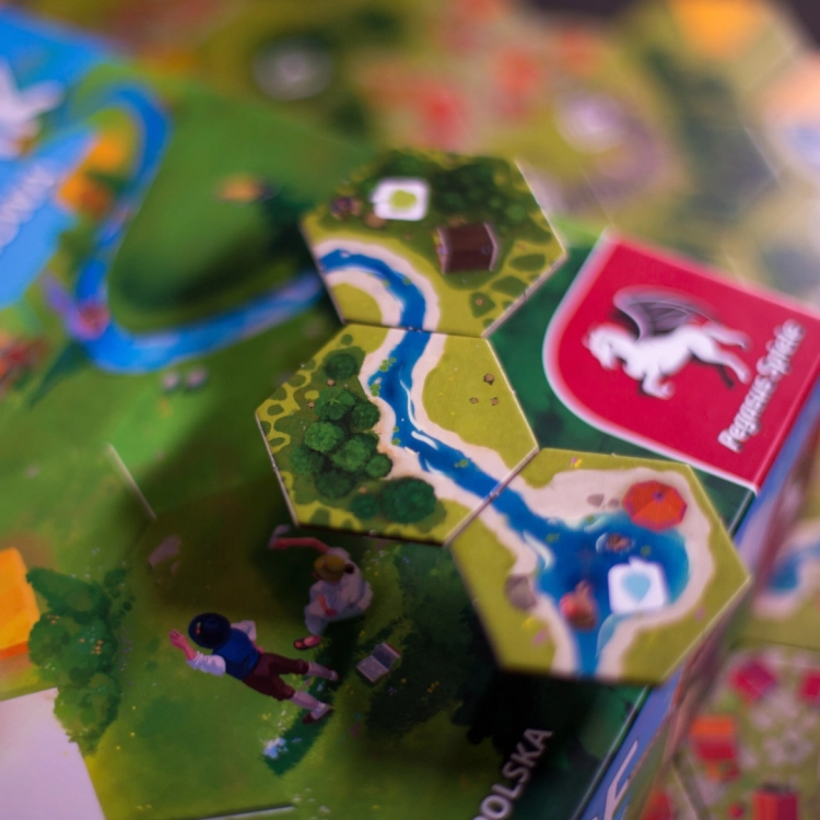 Kafelek z wodą w grze Dorfromantik – Ilustracja jeziora z plażą i postaciami pływającymi w wodzie.