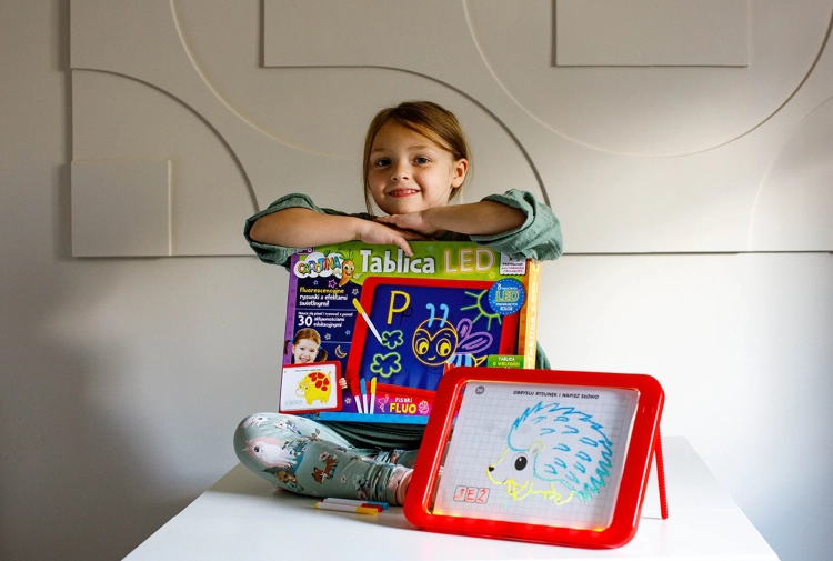 Dziewczynka prezentująca tablicę LED Carotina i jej opakowanie