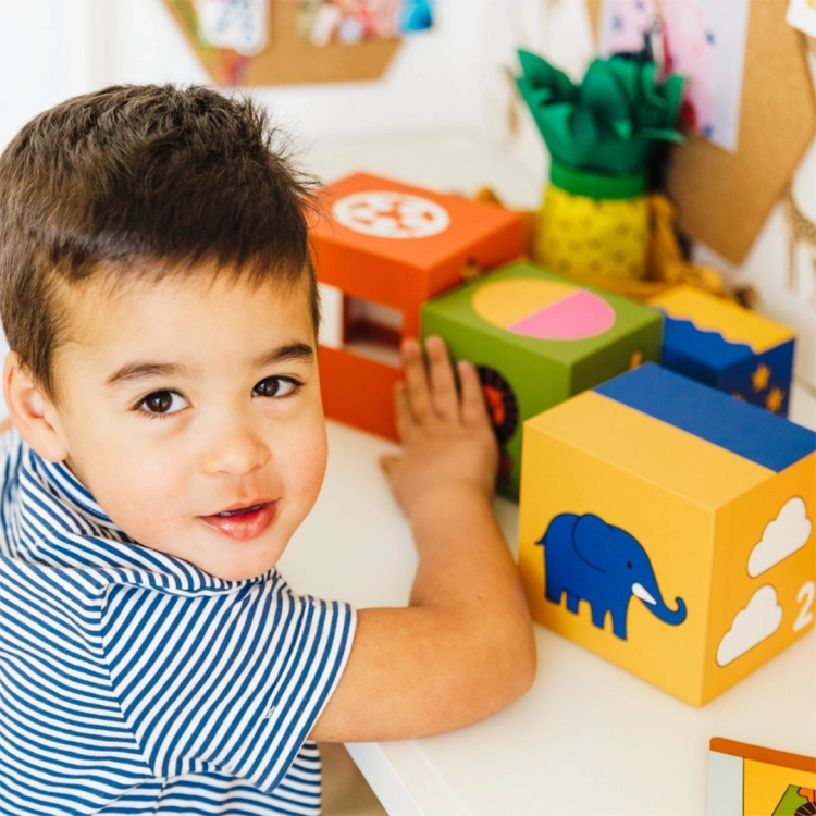 Dziecko bawiące się grą "A kuku! Zoo" SmartGames - chłopiec przy stole otoczony kolorowymi klockami z ilustracjami zwierząt.