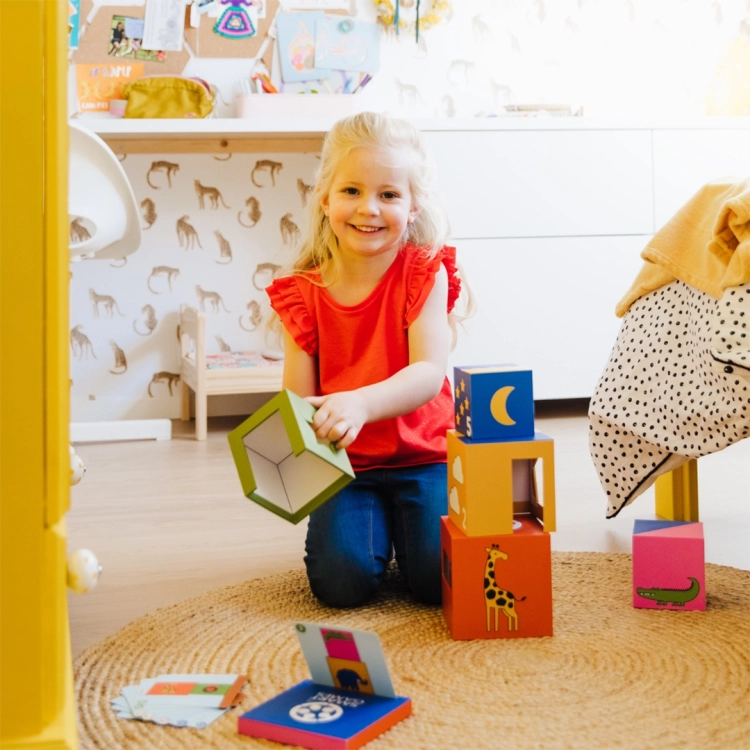 Zabawa grą logiczną "A kuku! Zoo" SmartGames 2+ - dziewczynka układająca wieżę z kolorowych klocków z motywem zwierząt.