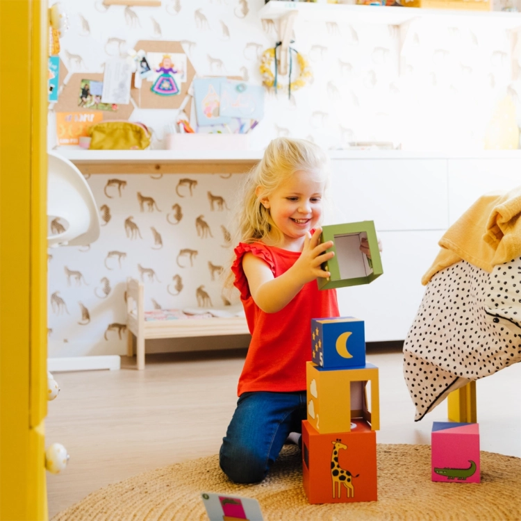 Dziecko układa klocki z gry "A kuku! Zoo" SmartGames - dziewczynka uśmiecha się, trzymając klocek i budując konstrukcję.