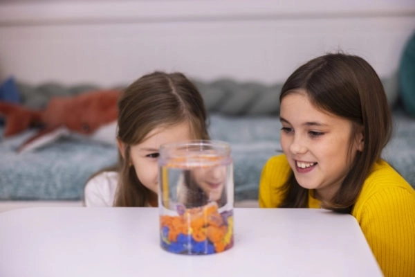 Dzieci obserwujące kolorowy piasek hydrofobowy przez przezroczyste akwarium z wodą.