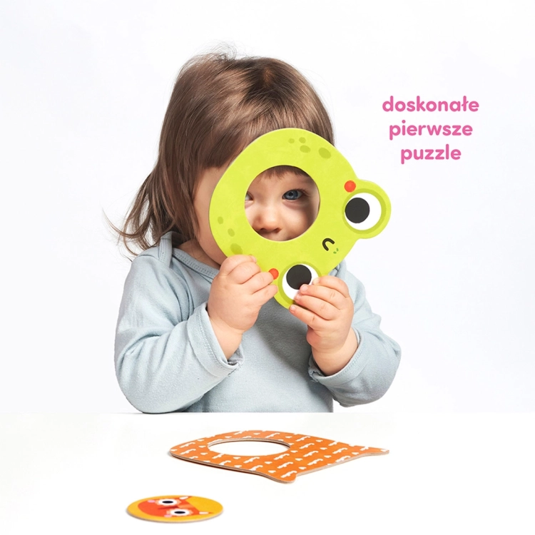 Dziecko patrzy przez otwór w zielonym puzzlu żabki z zestawu Moje puzzle z dziurką Zwierzątka.