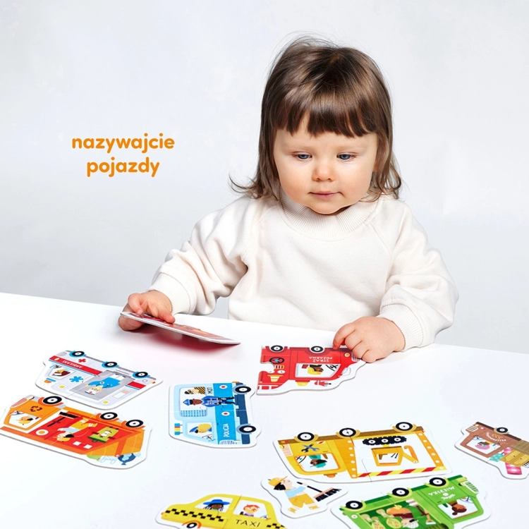 Dziewczynka bawi się puzzlami edukacyjnymi przedstawiającymi różne auta i zawody z nimi związane.
