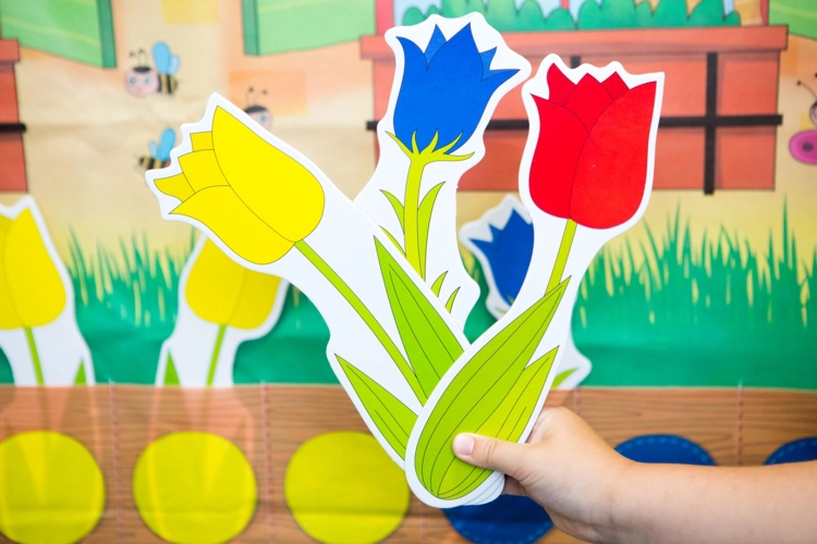 Kartki z kolorowymi tulipanami trzymane przez dziecko przed ścianą domku