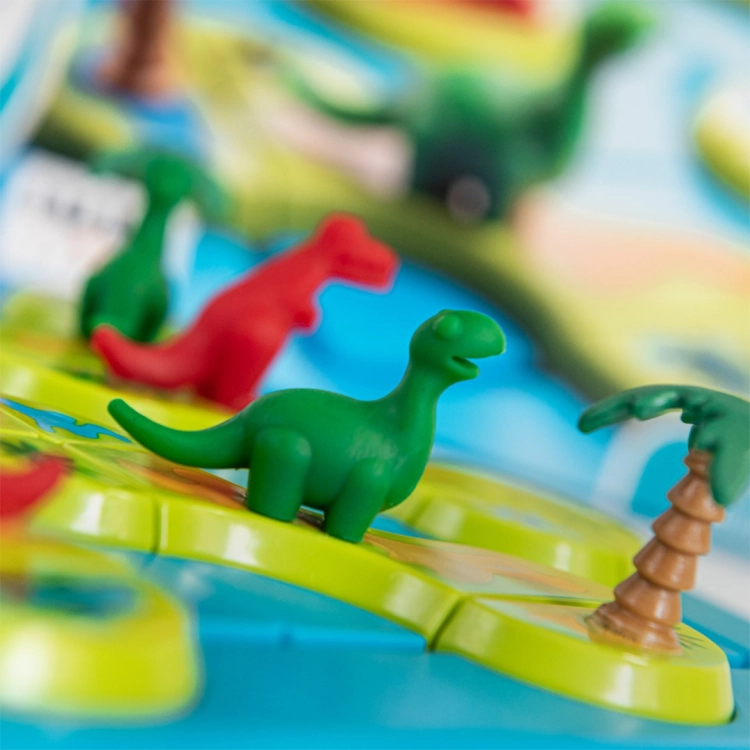Kilka figurek dinozaurów (zielonych i czerwonych) ustawionych na kolorowych segmentach planszy. Zbliżenie ukazuje detale wykonania postaci oraz elementów terenu.