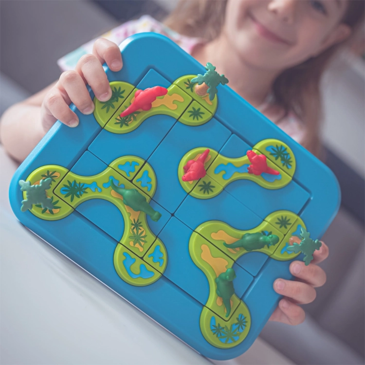 Dziewczynka prezentuje ułożoną planszę z grą logiczną Dinozaury – Tajemnicza Wyspa. Wszystkie elementy idealnie dopasowane, a postacie dinozaurów rozmieszczone zgodnie z zadaniem.
