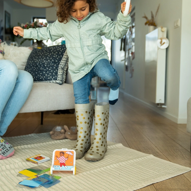 Dziecko w kaloszach odgrywa scenkę z gry Dress Code – ubieranie do deszczu.