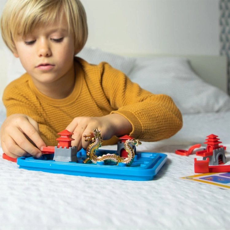 Chłopiec układa elementy gry Droga do Świątyni na łóżku – zabawa logiczna.