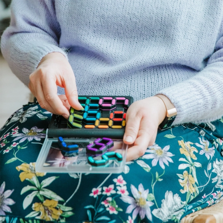 Osoba trzymająca grę IQ Digits na kolanach i dopasowująca elementy.