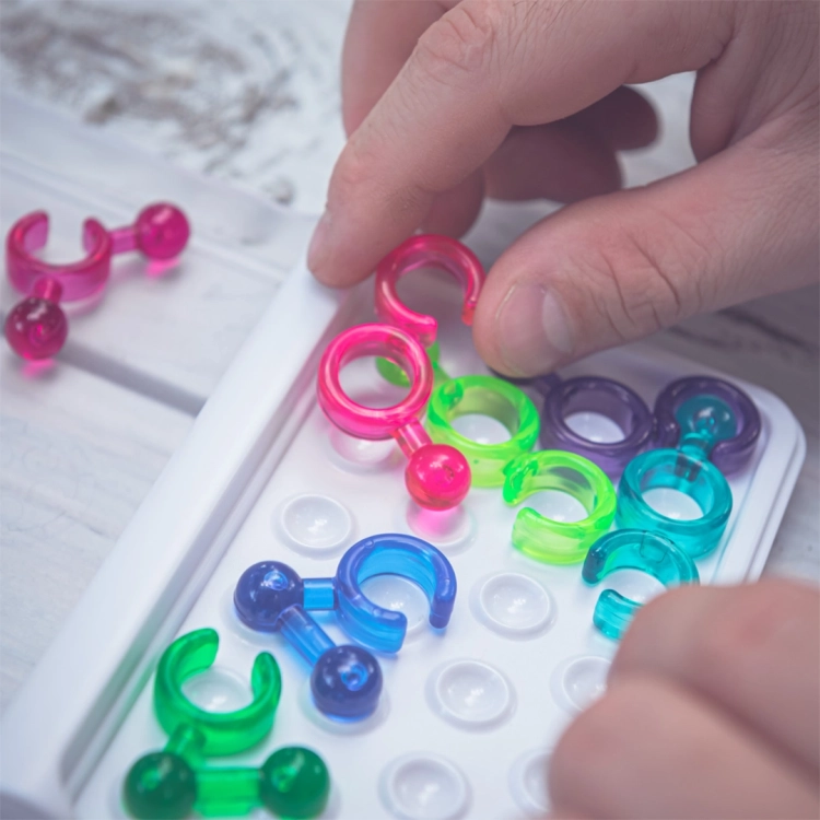 Zbliżenie na rękę układającą różowy element IQ Link na planszy.