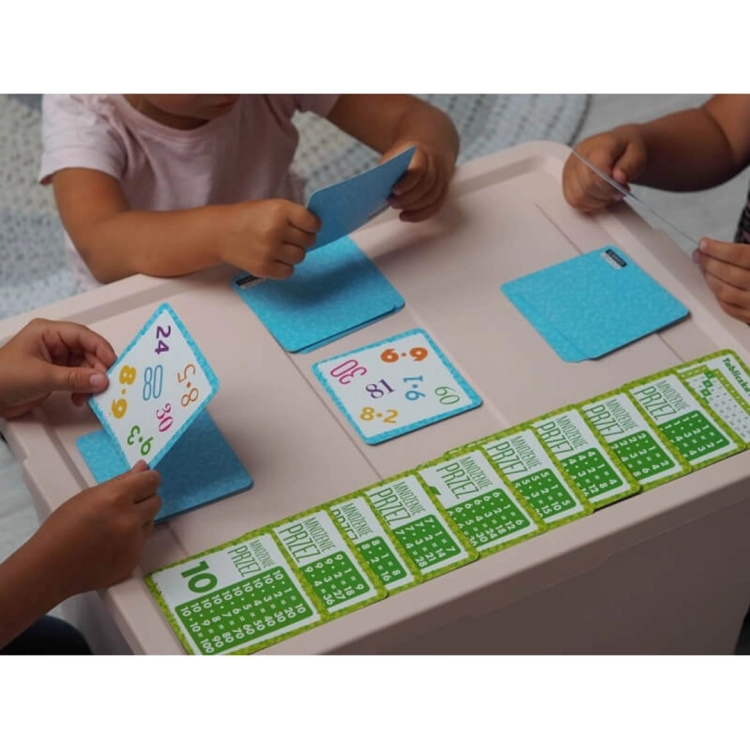 Dzieci grające w grę edukacyjną Bójka na mnożenie przy stole, karty z działaniami matematycznymi.
