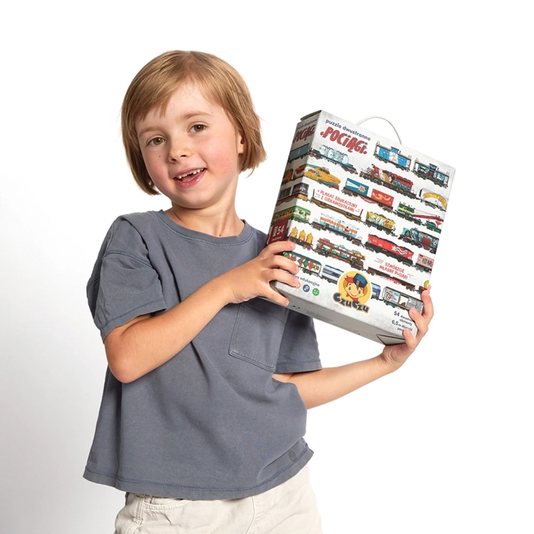 Dziecko trzymające pudełko puzzli dwustronnych Pociągi marki CzuCzu.