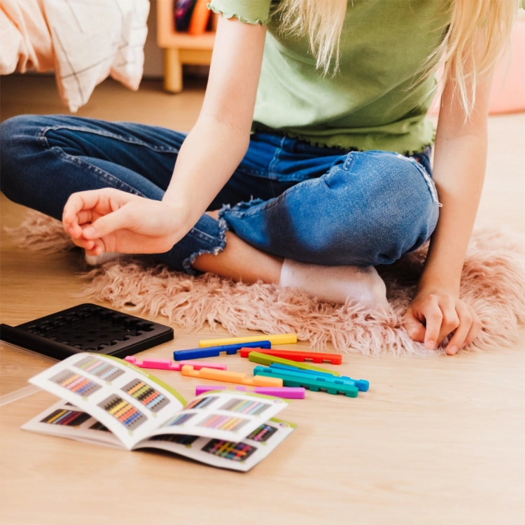 Dziewczynka układa kolorowe patyczki z gry IQ Stixx na dywanie.