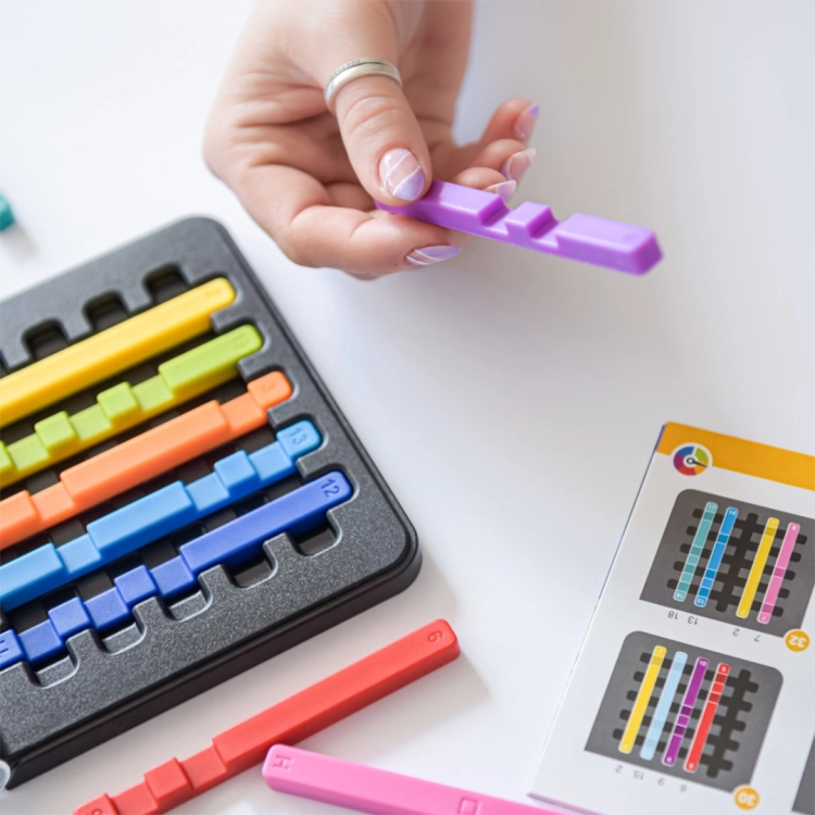 Ręka trzymająca fioletowy patyczek nad planszą IQ Stixx i instrukcją.