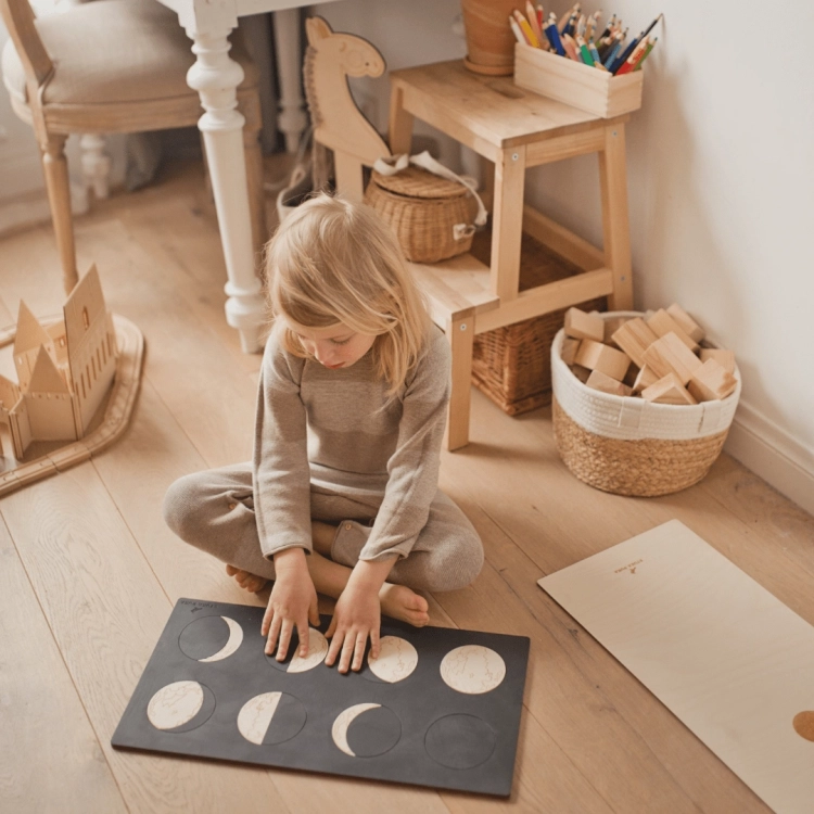 Dziewczynka układa puzzle fazy księżyca Sounds Wood w drewnianym pokoju Montessori