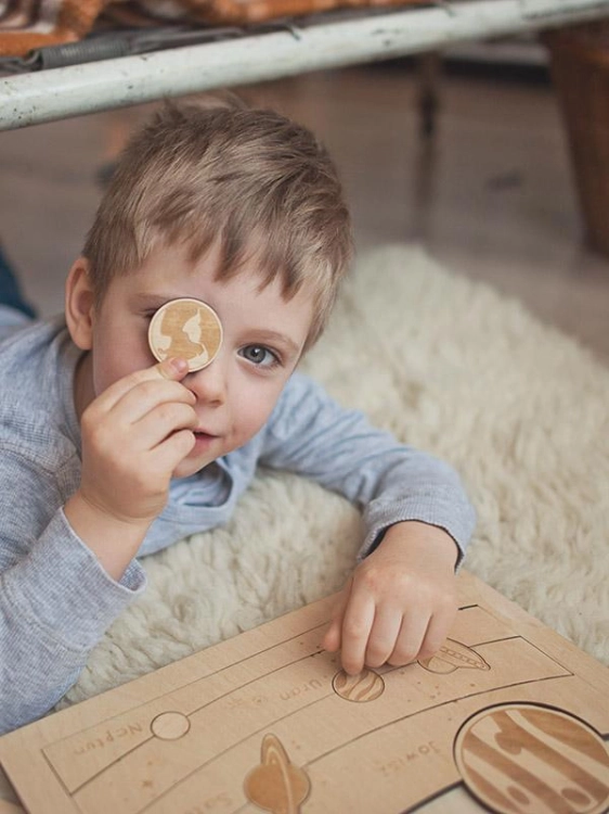 Chłopiec trzyma planetę Ziemię z drewnianych puzzli edukacyjnych o kosmosie