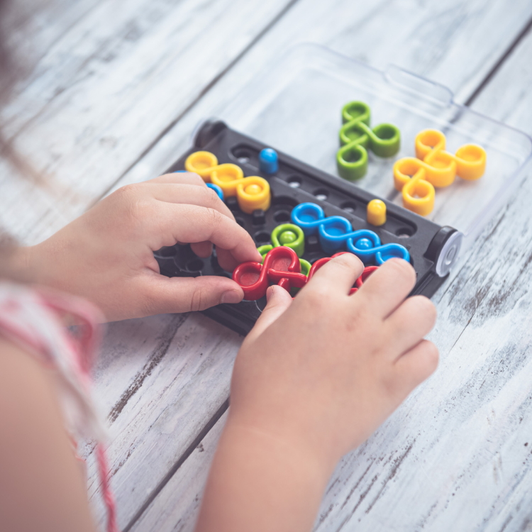 zbliżenie na dłonie dziecka układającego czerwony element iq twist