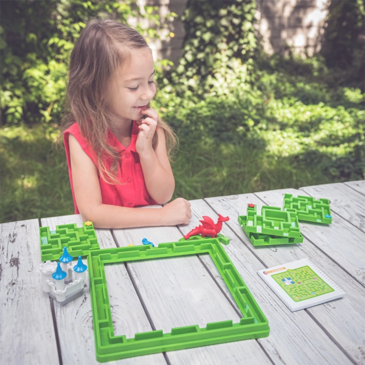 Dziewczynka układa grę Śpiąca Królewna Smart Games na stole w ogrodzie