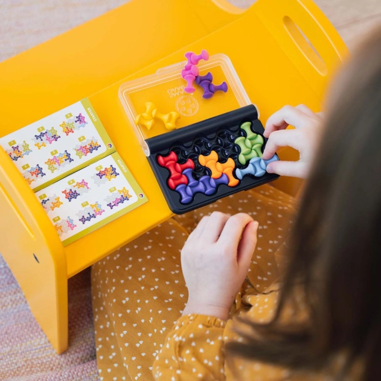 Dziecko układające kolorowe elementy gry IQ Waves na żółtym stoliku