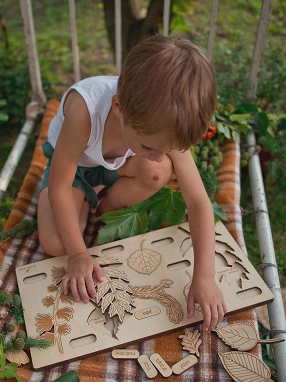 Chłopiec układa drewniane puzzle edukacyjne przedstawiające liście drzew