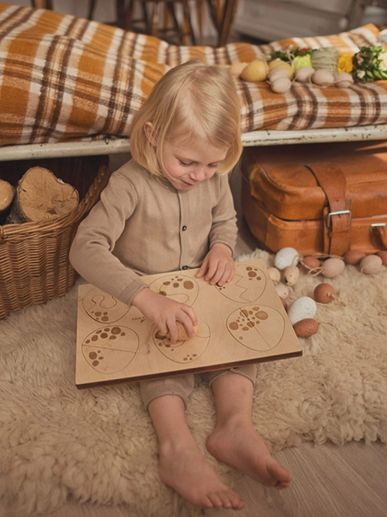 Dziewczynka układa puzzle drewniane z motywem jajek w siedzącej pozycji.