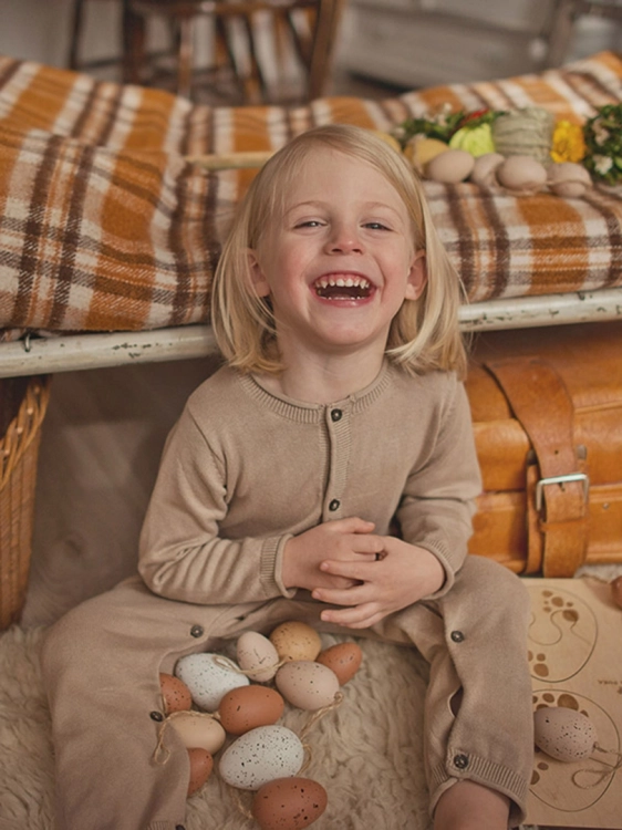 Uśmiechnięta dziewczynka siedzi wśród drewnianych jajek i puzzli Sounds Wood