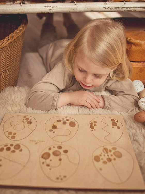 Dziewczynka leży i ogląda drewniane puzzle edukacyjne z jajkami.
