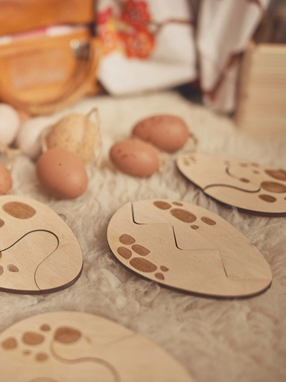 Drewniane puzzle w kształcie jajek obok dekoracyjnych jajek na dywanie.