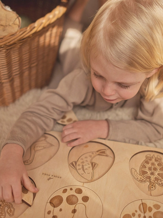 Dziewczynka układa puzzle z rybą, żółwiem i wężem z zestawu Sounds Wood