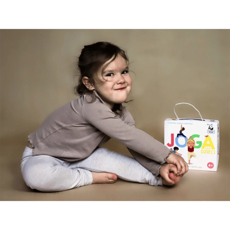 Dziewczynka wykonująca pozycję jogi z pudełkiem Joga dla dzieci obok