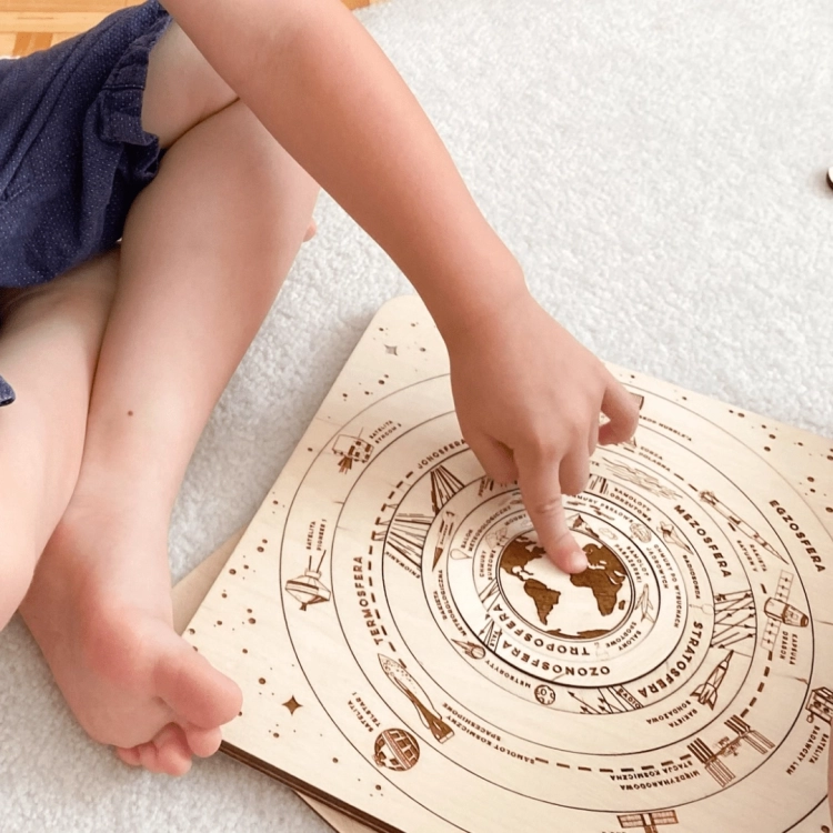 Dziecko bawiące się drewnianymi puzzlami przedstawiającymi warstwy atmosfery