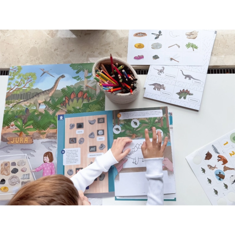 Dziecko pracujące z zestawem Teczka Montessori 4 lata – plansze, naklejki i elementy z dinozaurami.