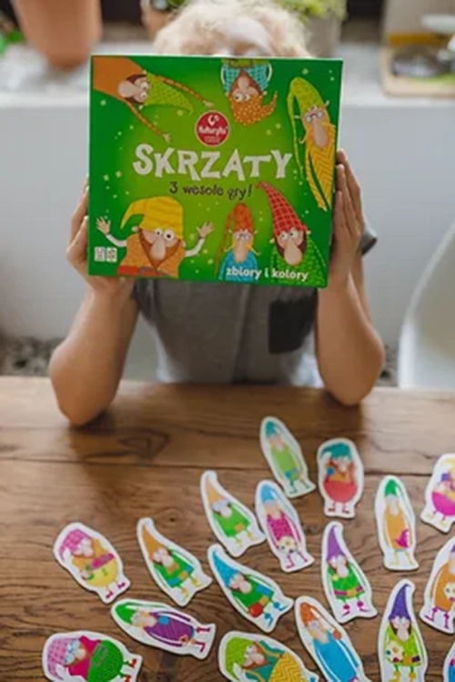 Dziecko trzyma pudełko gry Skrzaty 3 wesołe gry Kukuryku