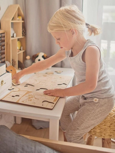 Dziewczynka układa drewniane puzzle ze zwierzętami na białym stoliku.