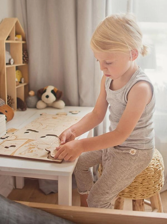 Blondwłosa dziewczynka siedzi przy stoliku i bawi się edukacyjnymi puzzlami ze zwierzętami.