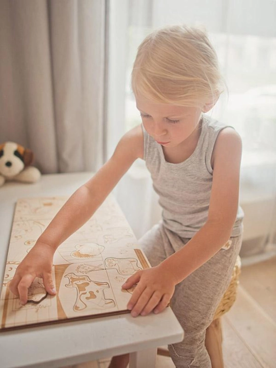 Dziecko z zainteresowaniem wkłada element do drewnianej układanki ze zwierzętami.