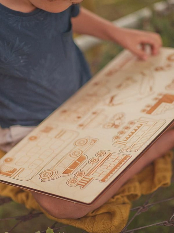 Dziecko bawi się drewnianymi puzzlami z pojazdami na zewnątrz.