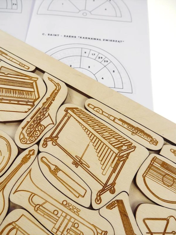 Fragment drewnianej układanki z instrumentami oraz ulotką z opisem "Karnawału zwierząt".