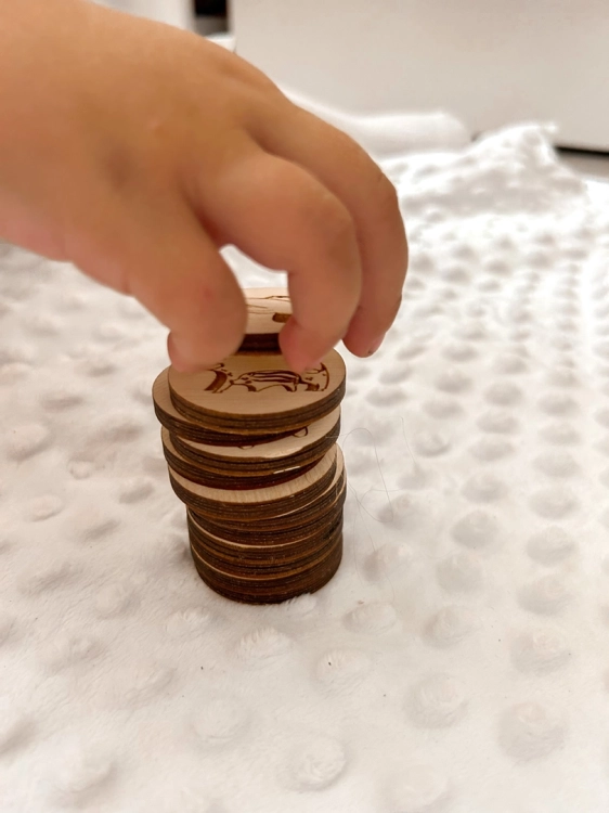 Dłoń dziecka układająca drewniane kółka z owadami do gry memory Sounds Wood