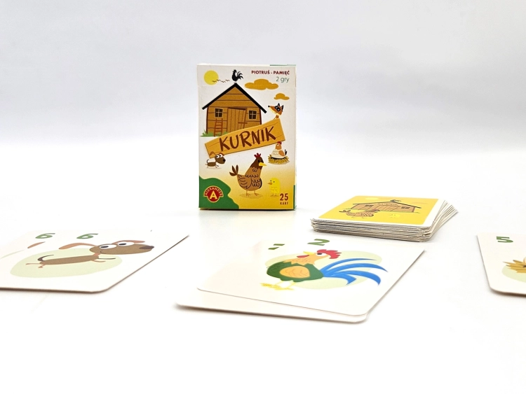 Pudełko gry karcianej Piotruś Pamięć Kurnik na białym tle, otoczone rozłożonymi kartami z ilustracjami zwierząt.